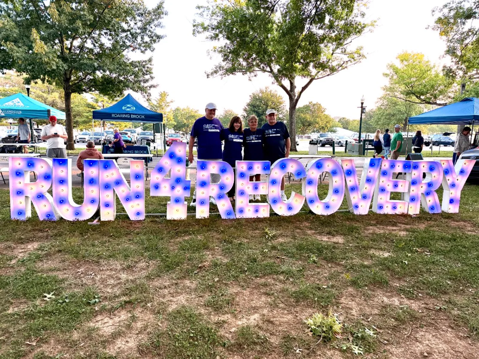 Run for Recovery participants gathered around the illuminated RUN 4 RECOVERY marquee sign at Keeneland